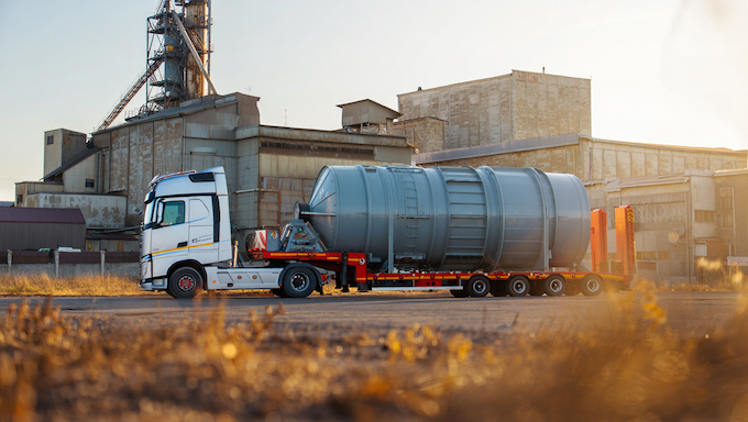 Moderner LKW mit überdimensionalem Silo auf einem Tieflader, bereit zur Entladung in einem Industriegebiet am Stadtrand von Kasachstan, bei spätherbstlichem Sonnenlicht
